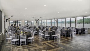 A large indoor venue with multiple round tables and chairs, large windows with a view of a body of water and hills, and a modern ceiling design. - Home2 Suites By Hilton Guntersville (Guntersville)