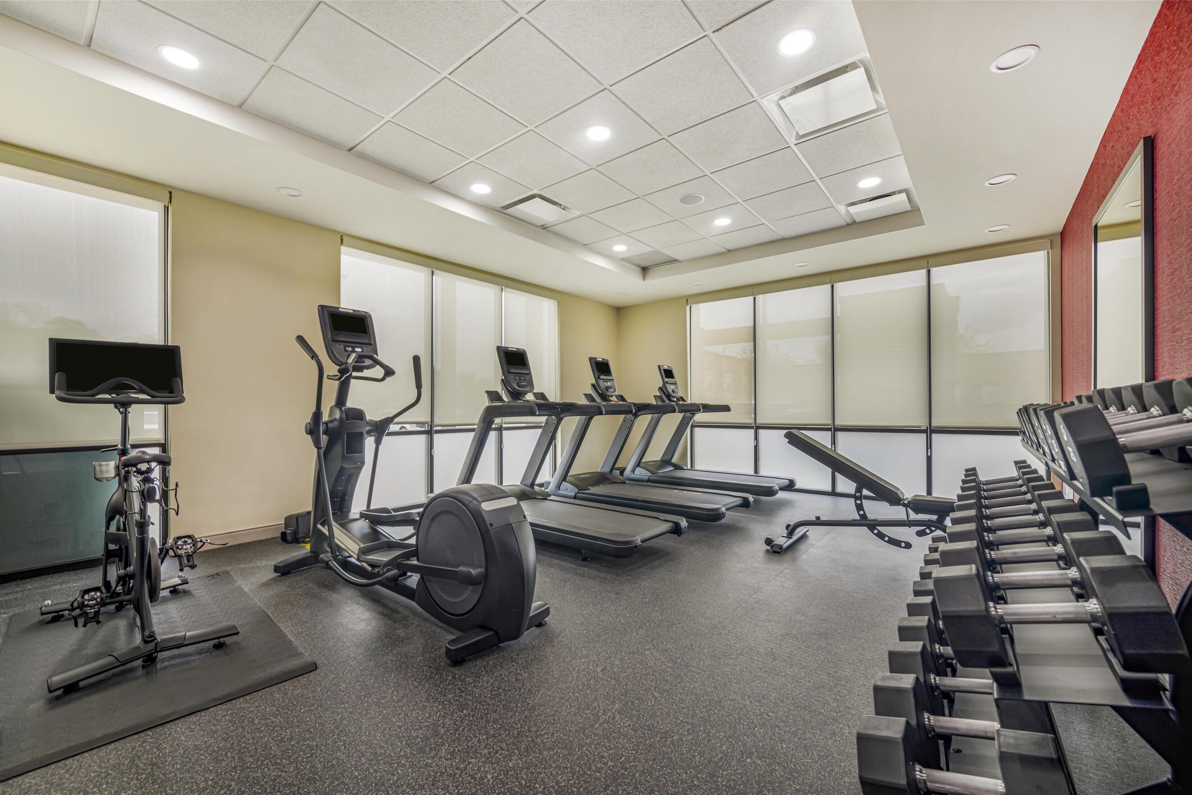 Un gimnasio con cintas de correr, elípticas y una máquina de remo.