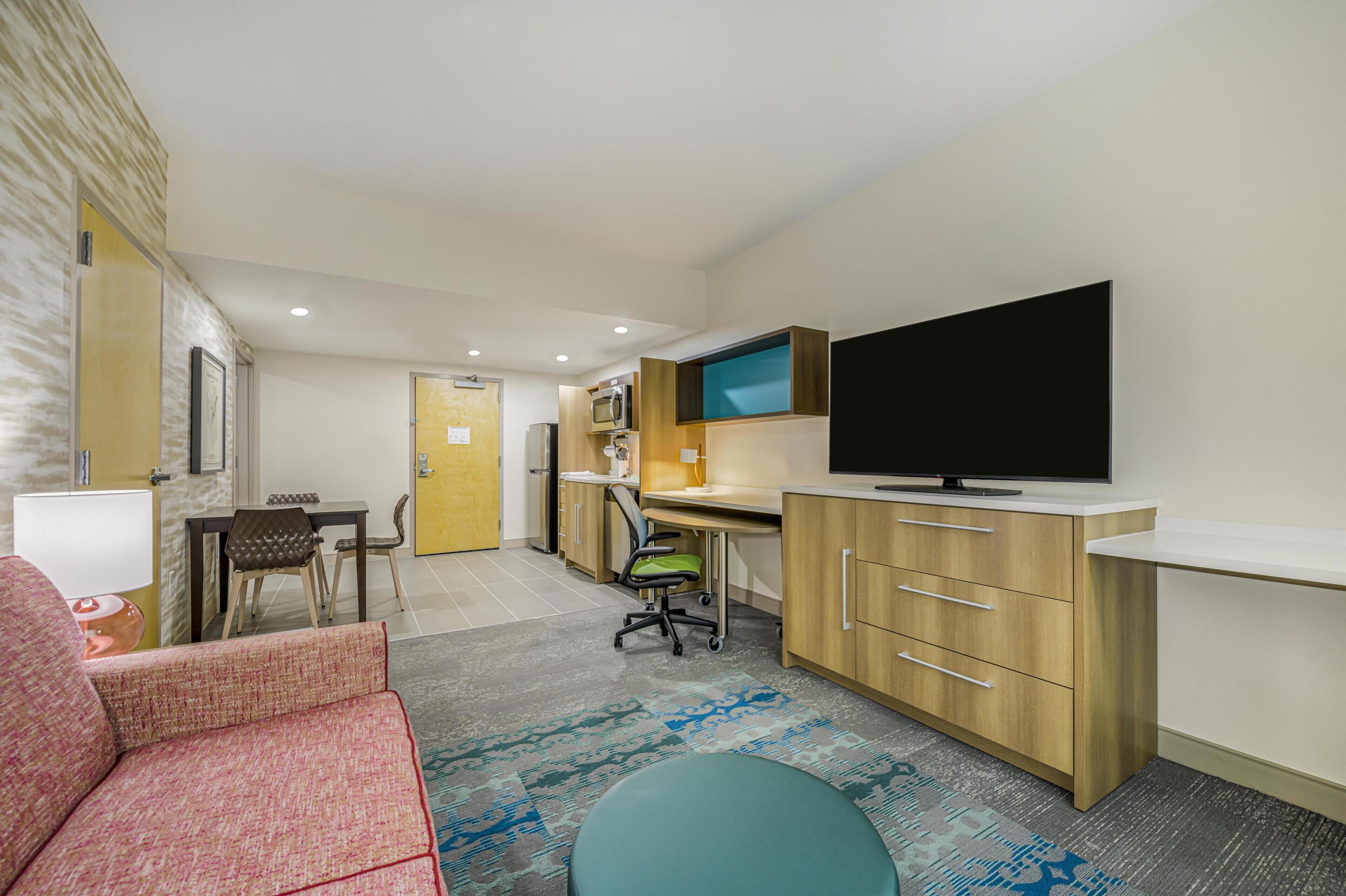 Une chambre d’hôtel compacte comprenant un coin cuisine, un espace repas, une télévision et un coin salon avec un canapé et une petite table ronde.