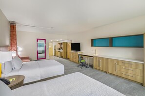 Habitación de hotel con dos camas, un escritorio, un televisor y un baño visible a través de una puerta abierta.