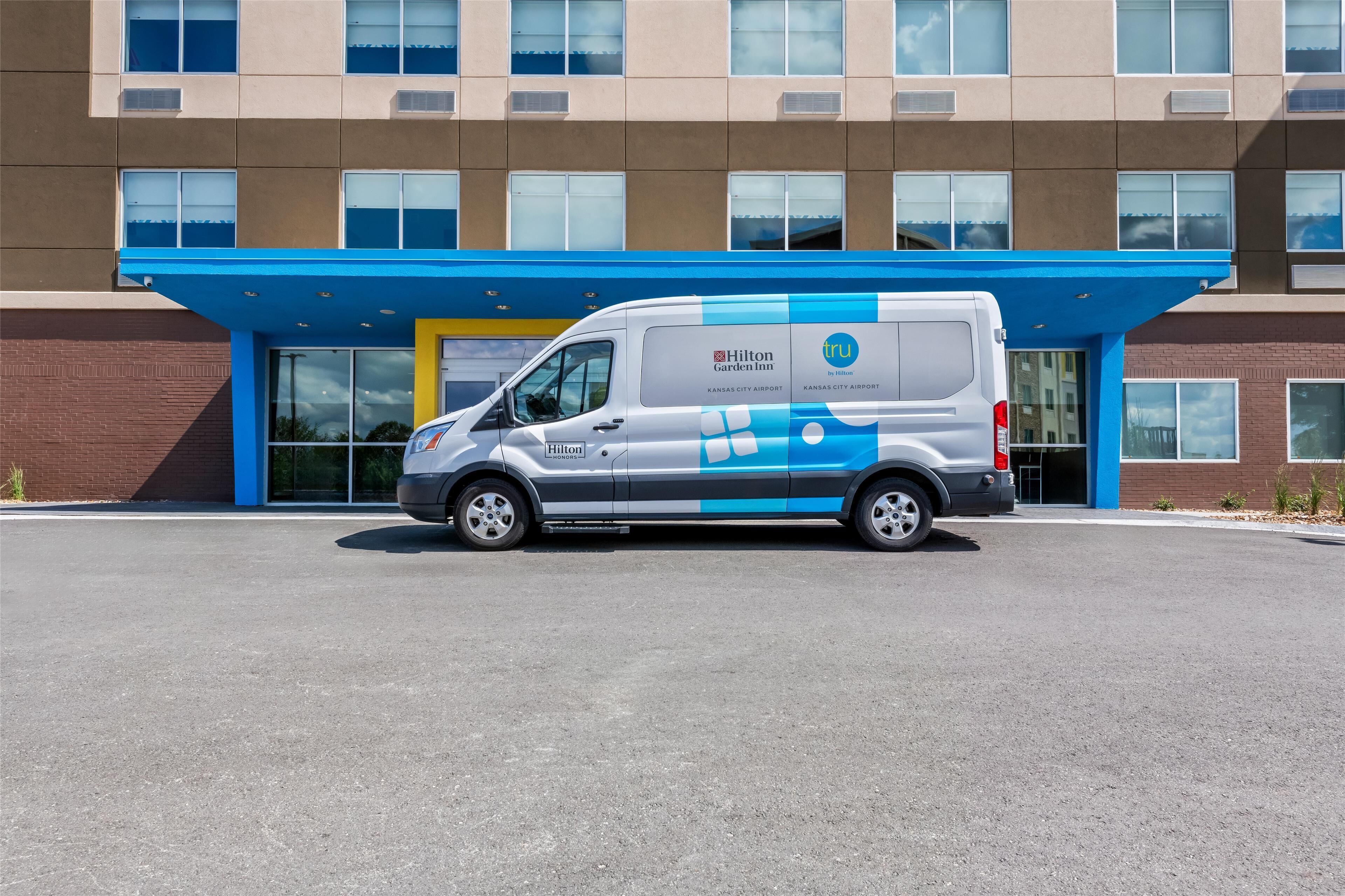 Una camioneta blanca estacionada frente a un edificio con toldo azul y un amplio acceso de vidrio.