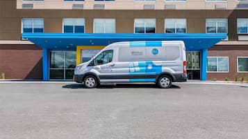 A white van parked in front of a building with a blue awning and a large glass entrance.
