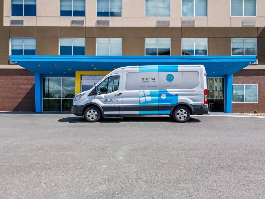 A white van parked in front of a building with a blue awning and a large glass entrance.