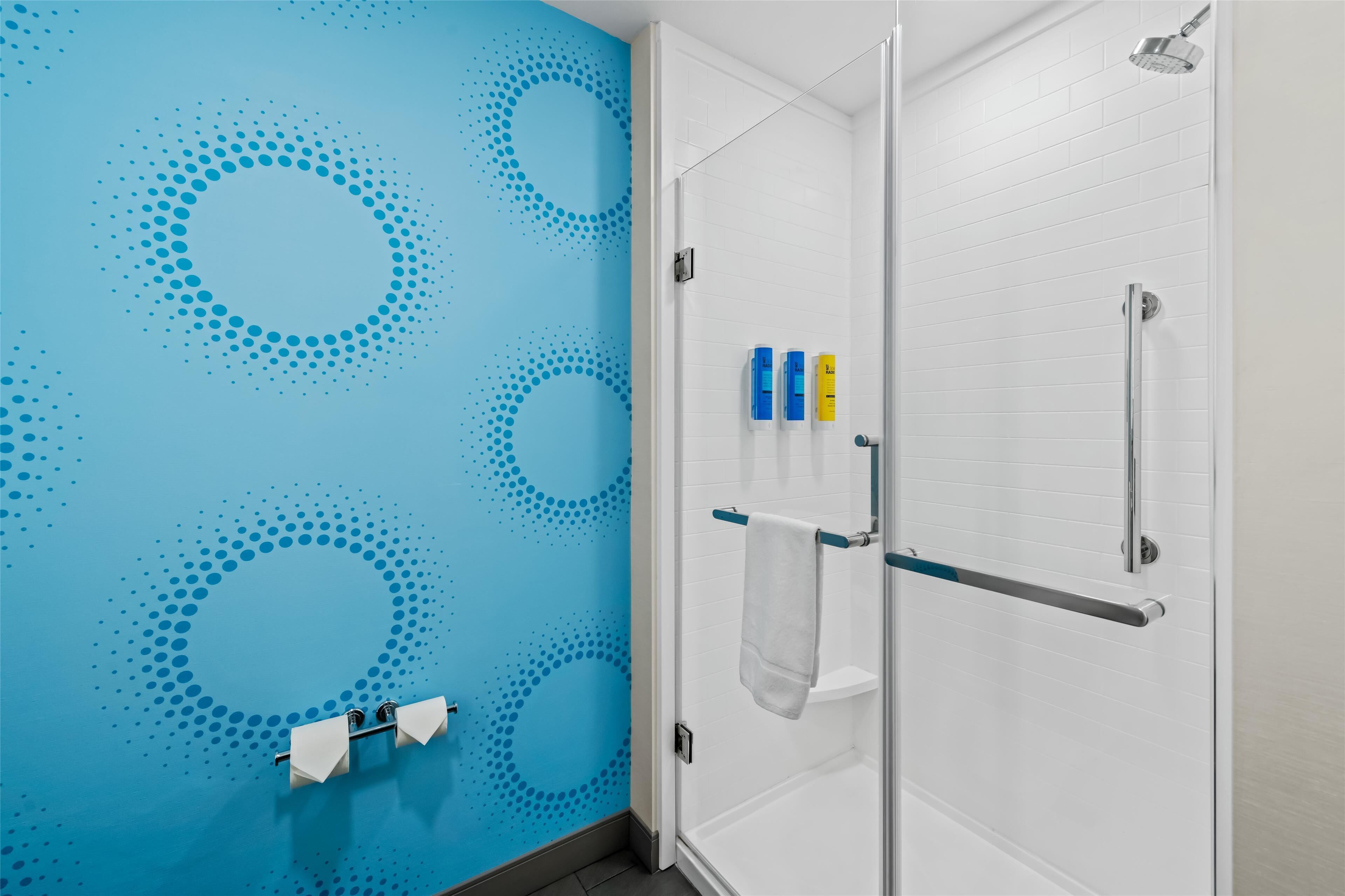 Casa de banho com parede azul com padrão de pontos, cabine de duche em vidro e suporte de toalhas com uma toalha branca.