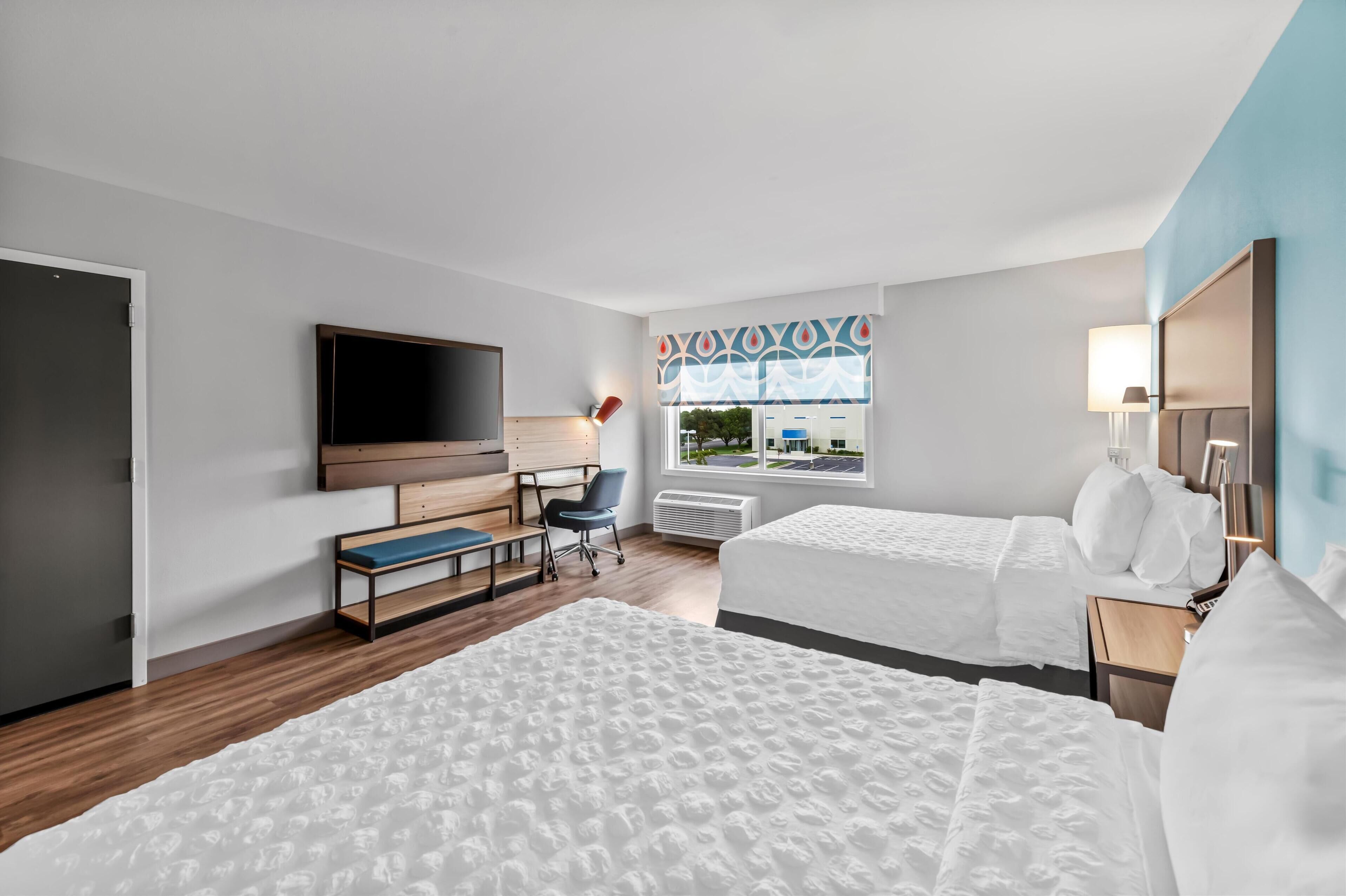 Habitación de hotel con dos camas, un escritorio, una silla, un televisor y una ventana con cortinas estampadas.