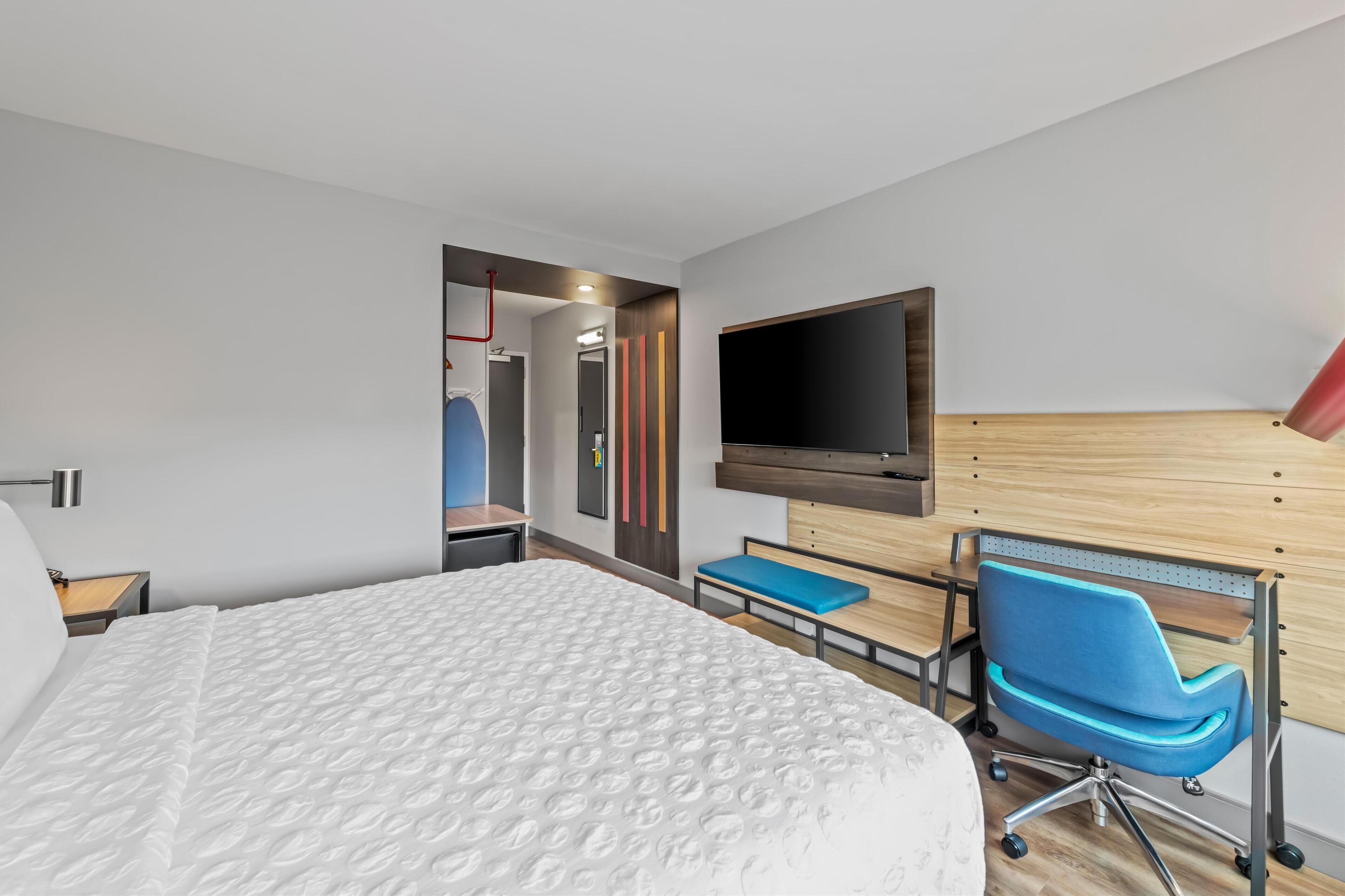 Moderni hotellihuone, jossa on suuri sänky, työpöytä, tuoli, televisio ja puinen pääty.