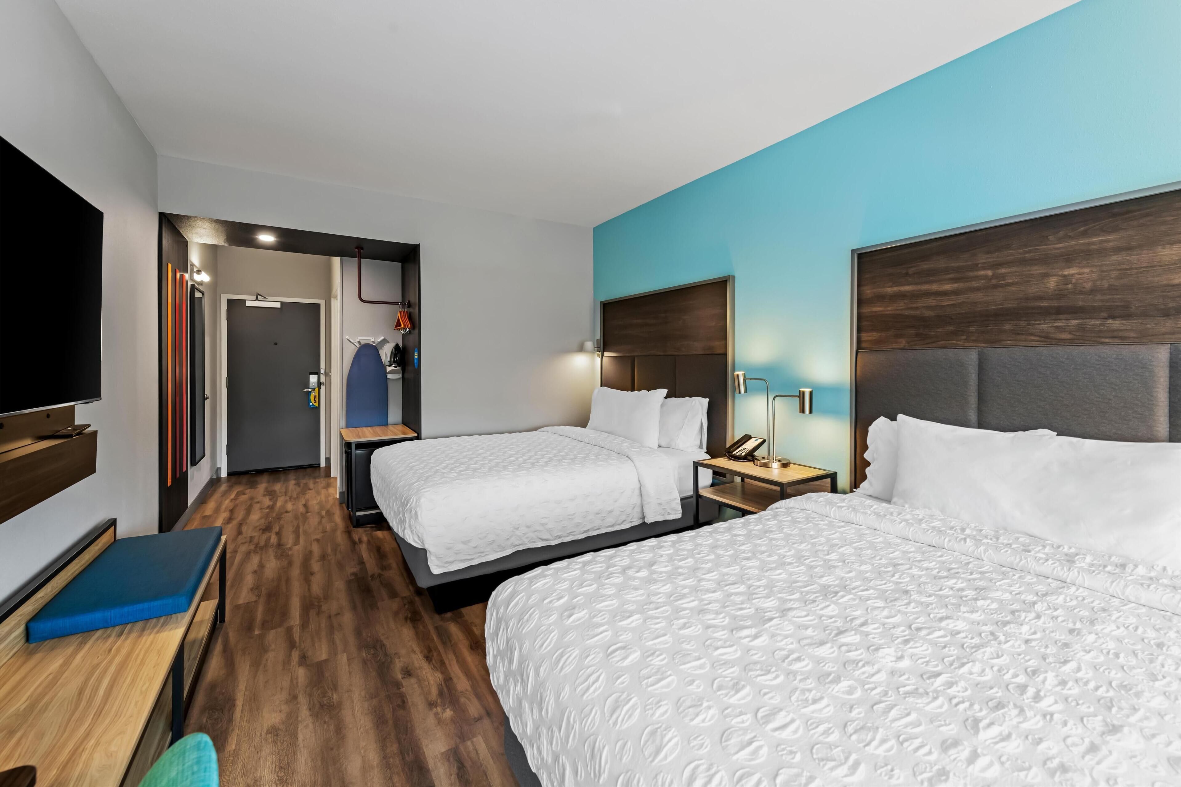 A hotel room with two beds, a desk, a TV, and a bathroom visible through an open door.