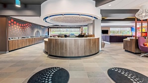 A modern reception area with a central counter, seating, and a decorative ceiling. - Tru By Hilton Kansas City Airport (Kansas City)