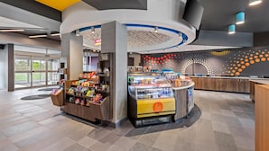 A modern retail area with a snack kiosk, a refrigerated display, and a counter with beverages. - Tru By Hilton Kansas City Airport (Kansas City)