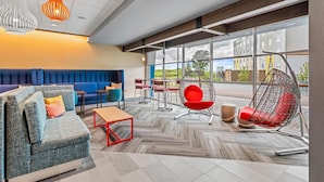 A modern lounge area with a blue sofa, red chair, and a hanging egg chair. - Tru By Hilton Kansas City Airport (Kansas City)