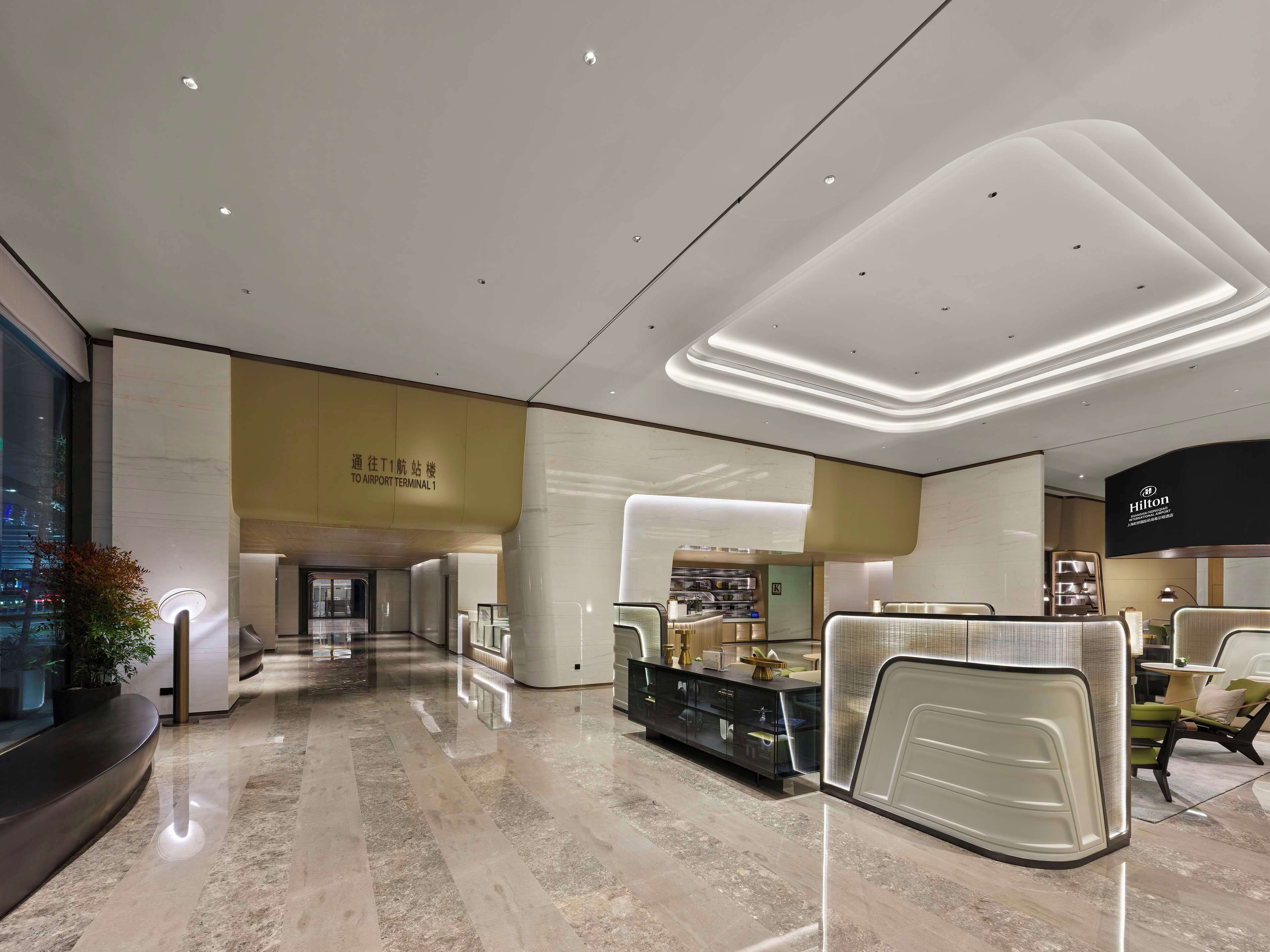 A modern hotel lobby with a marble floor, a reception desk, and a visible Hilton sign.
