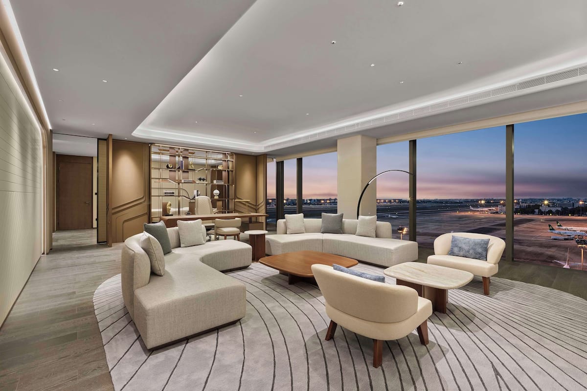 Eine moderne Hotellobby mit einer gebogenen Eckcouch, einem runden Couchtisch und Blick auf den Flughafen.