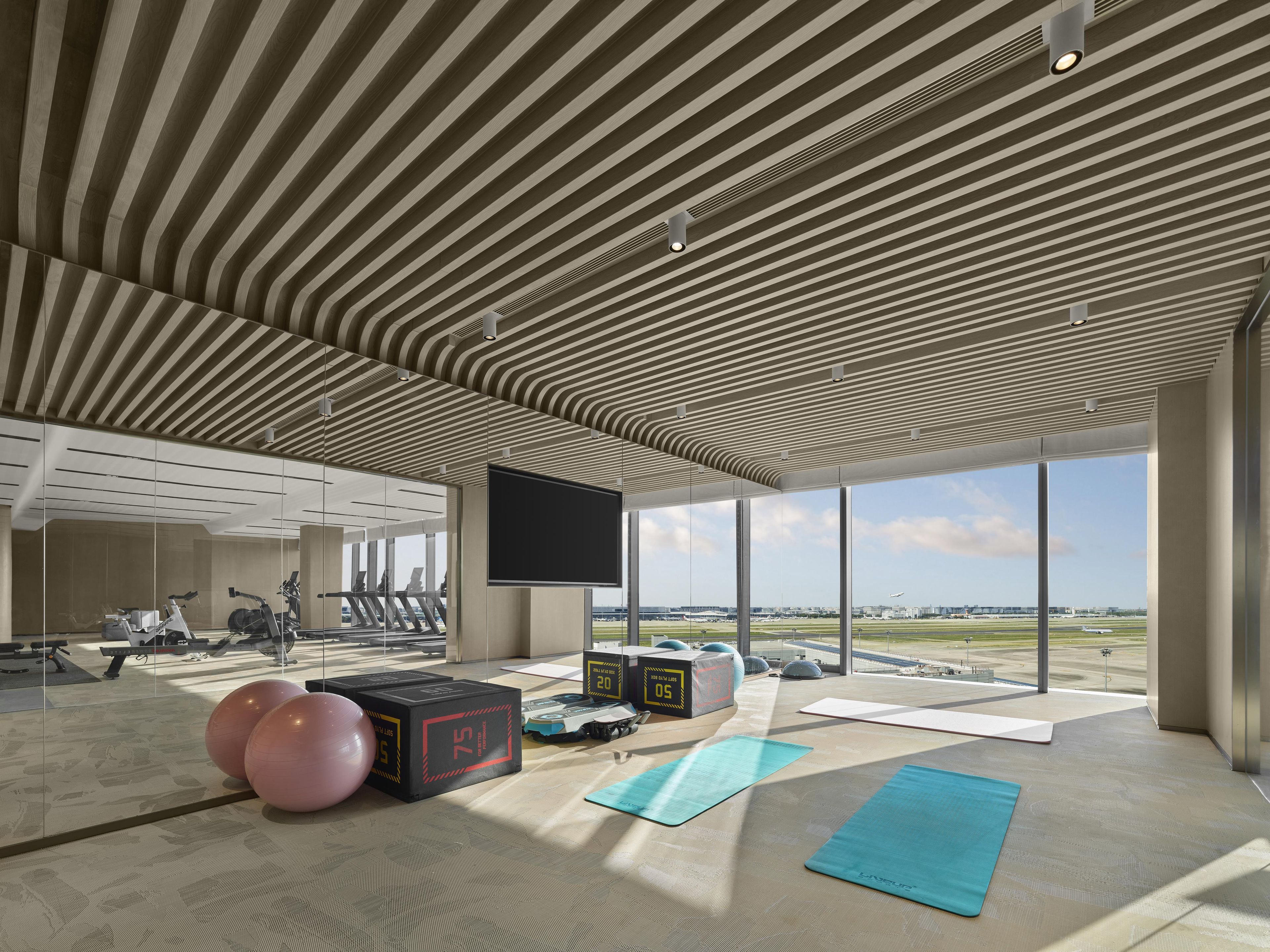 Un gimnasio moderno con equipamiento de ejercicio, ventanas amplias y vistas al aeropuerto.