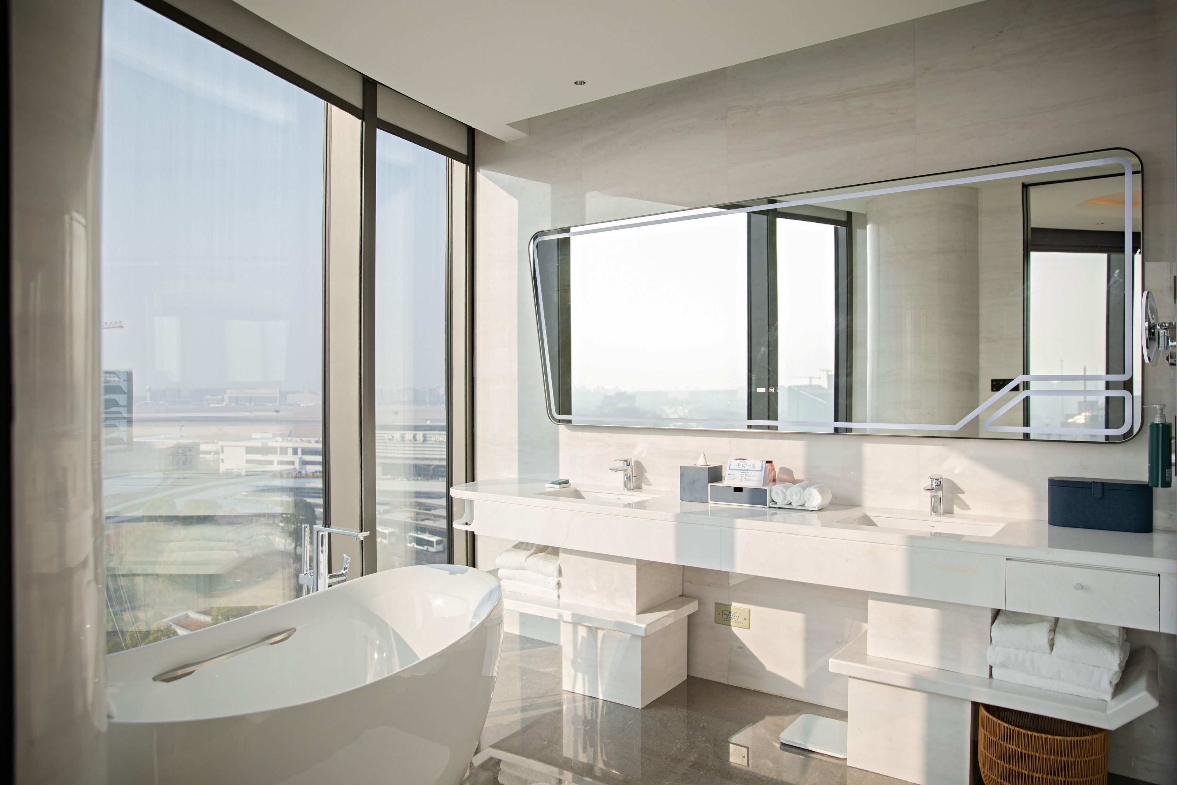 A modern bathroom with a large bathtub, dual sinks, and a large mirror.