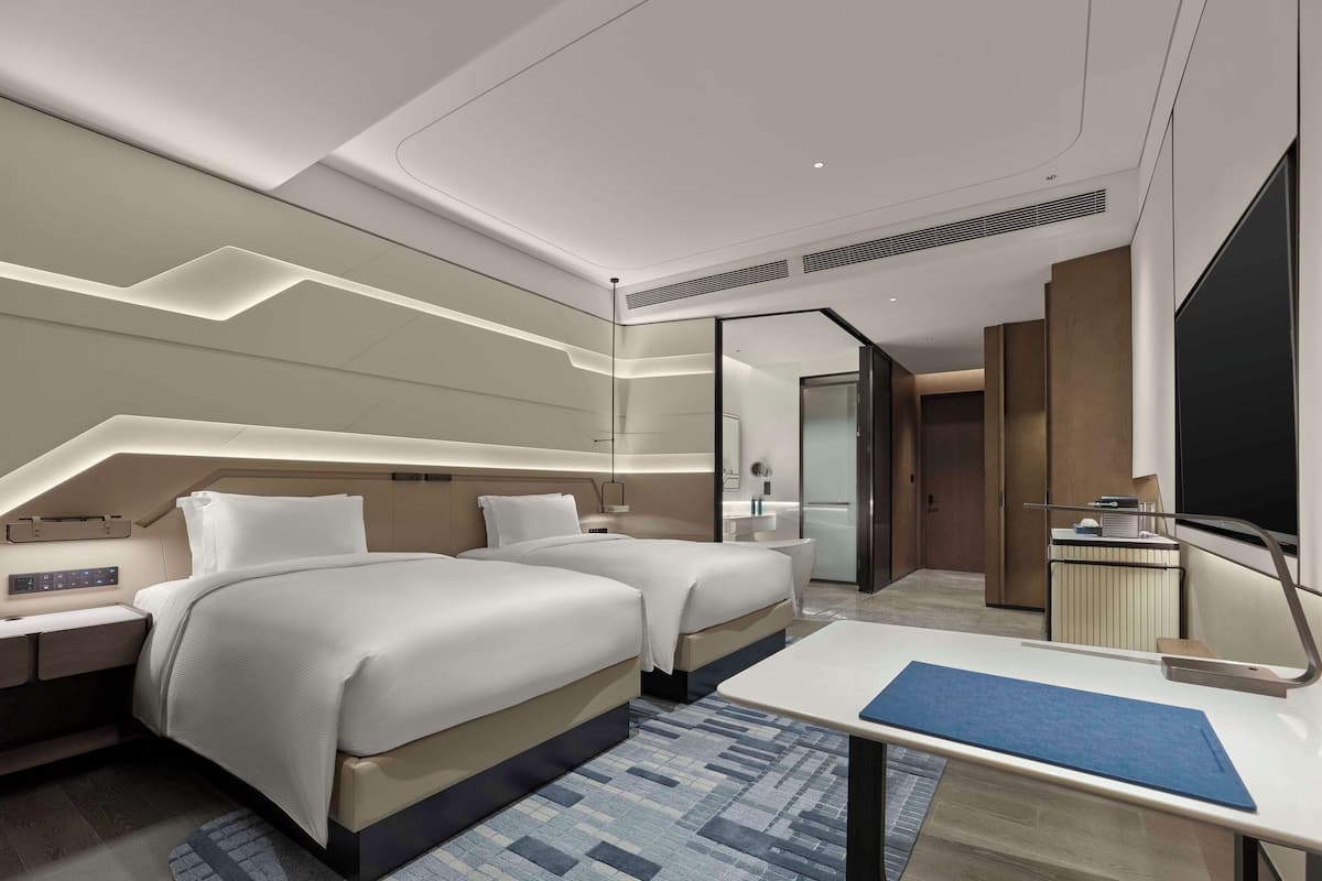 Ein modernes Hotelzimmer mit zwei Betten, einem Schreibtisch, einem großen Spiegel und einem begehbaren Kleiderschrank.
