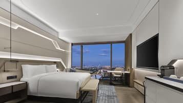A modern hotel room with a large bed, bedside tables, a desk, a chair, and a TV.
