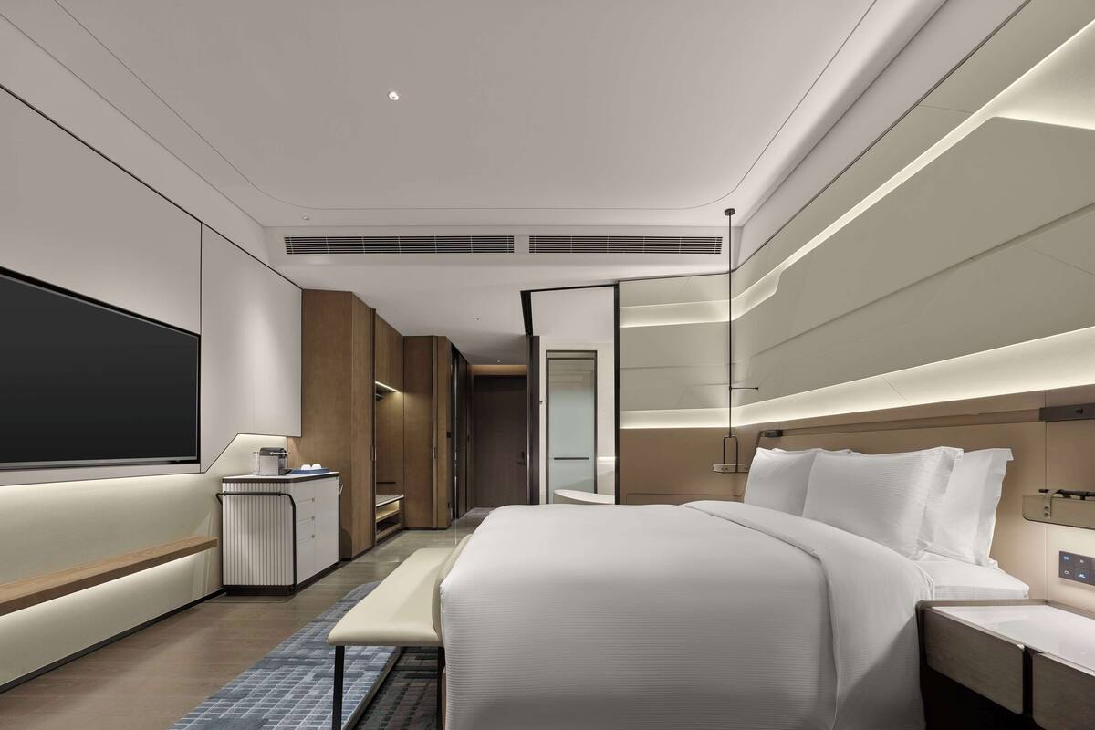 Ein modernes Hotelzimmer mit einem großen Bett, Nachttischen, einem Schreibtisch, einem Fernseher und einem Badezimmer mit Dusche und Toilette.