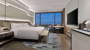 Una habitación de hotel moderna con una cama grande, mesitas de noche, un escritorio con silla, un televisor y vistas a la ciudad.