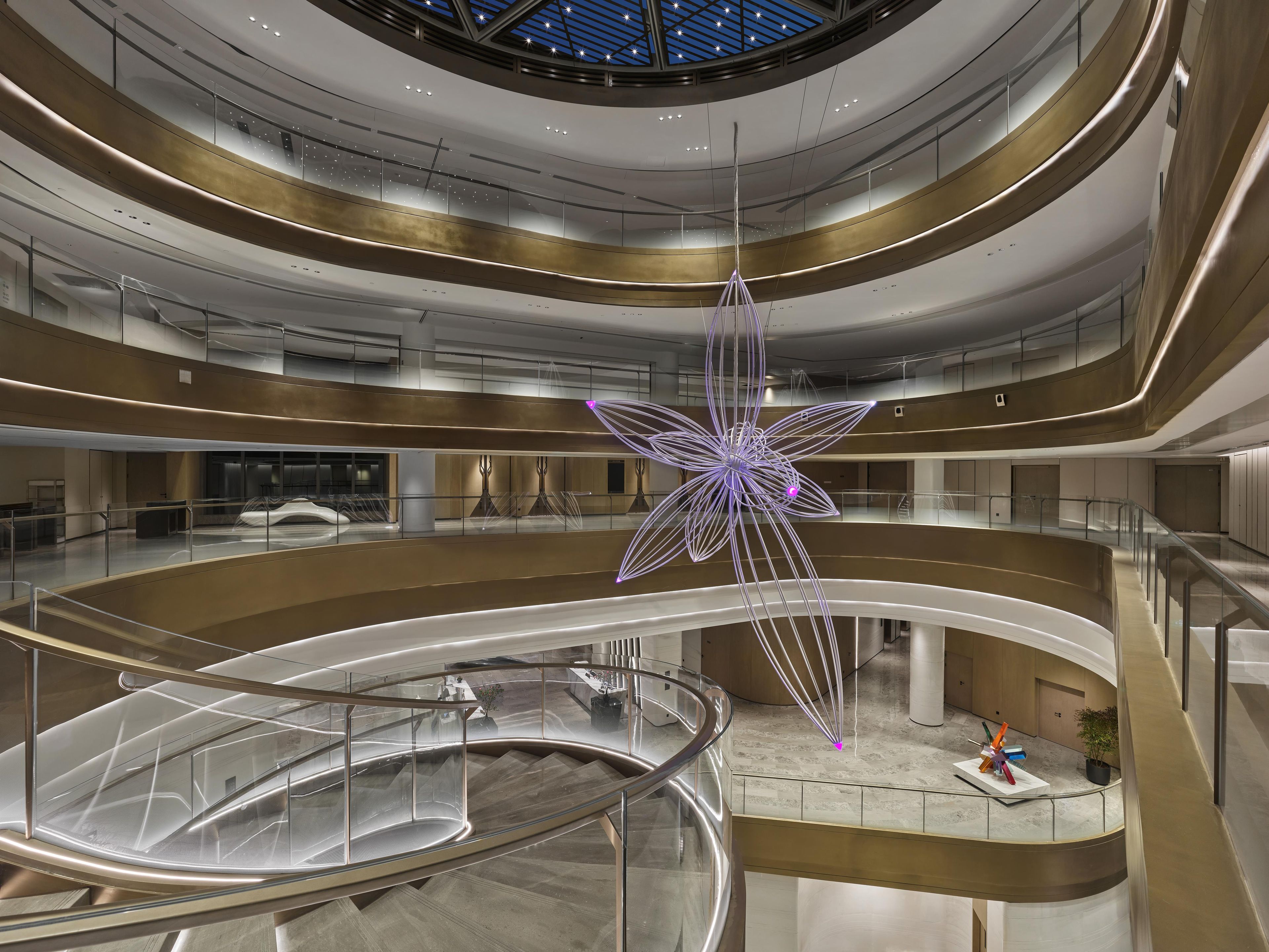 A multi-level atrium with a central staircase, glass railings, and a large hanging sculpture.