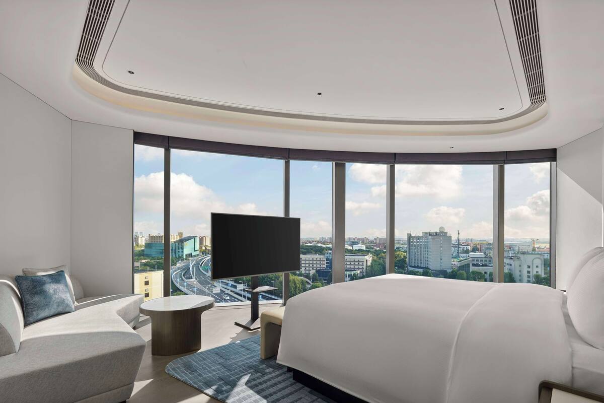 Ein modernes Hotelzimmer mit einem großen Bett, einer Couch, einem Fernseher und Blick auf die Stadt.