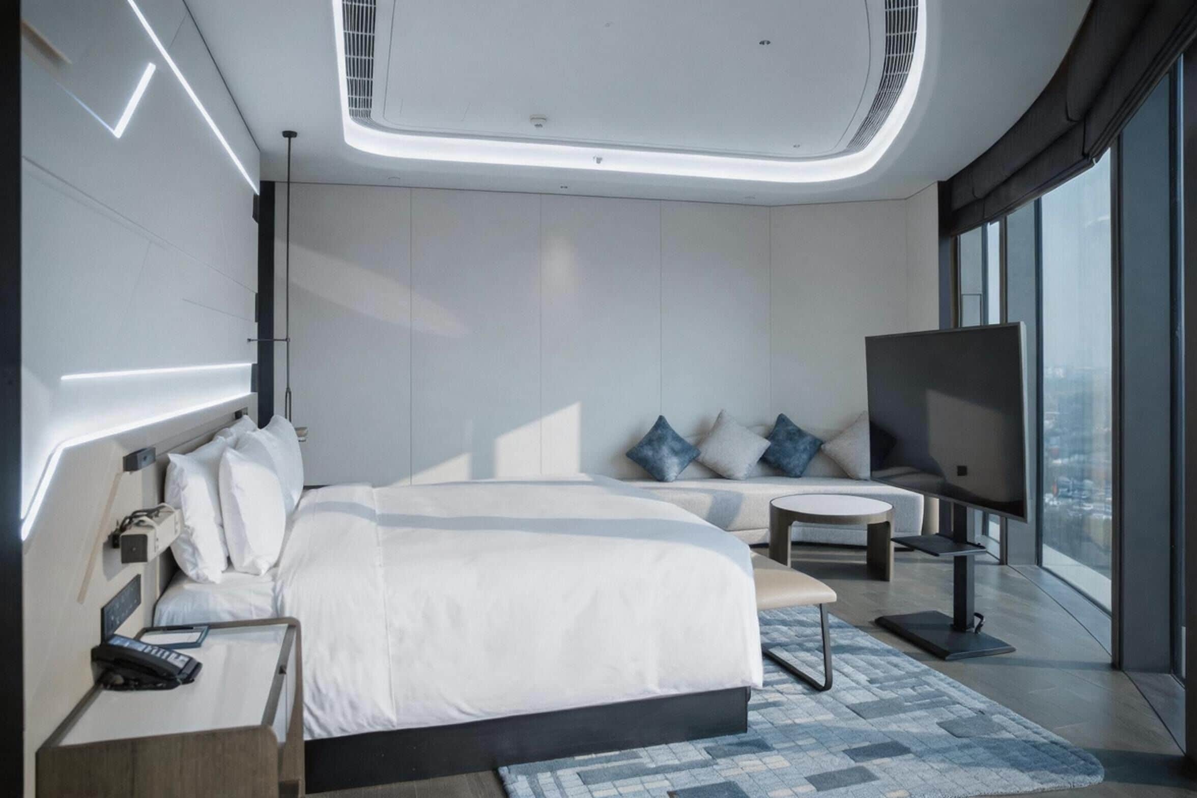 Ett modernt hotellrum med en stor säng, en TV, ett litet bord och utsikt över staden.