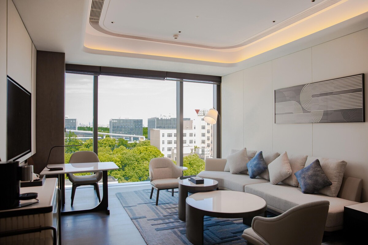Una habitación de hotel moderna con un ventanal grande, un sofá, un escritorio y un televisor.