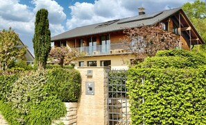 A two-story house with a stone wall entrance, a balcony, and a well-maintained garden.
