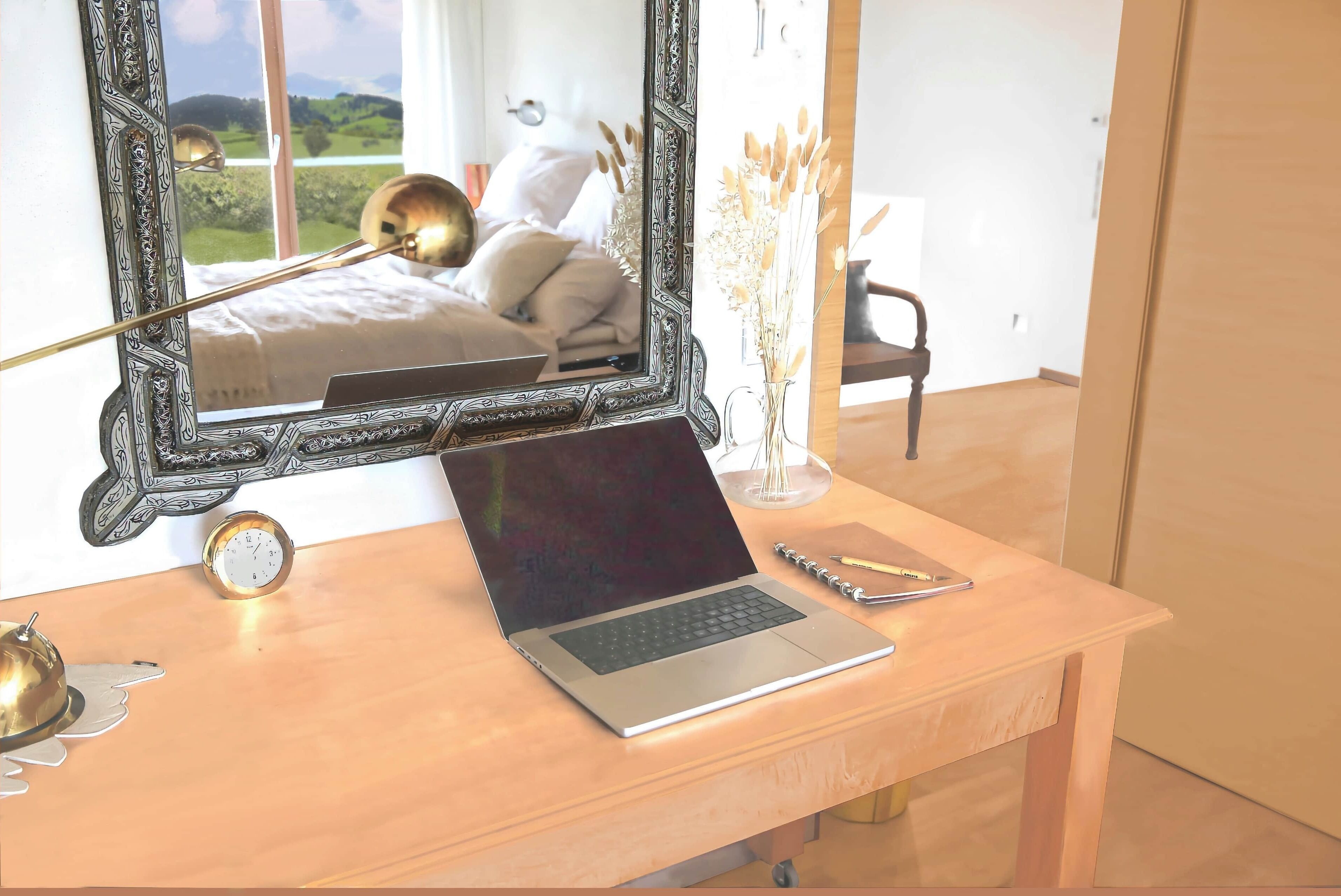 A wooden desk with a laptop, a clock, and a vase with dried plants.