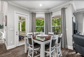 Un comedor con una mesa de madera y sillas blancas, una parrilla y vistas a la vegetación.