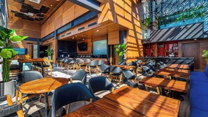 A modern indoor seating area with wooden tables and chairs, a bar area, and a large flat-screen TV.