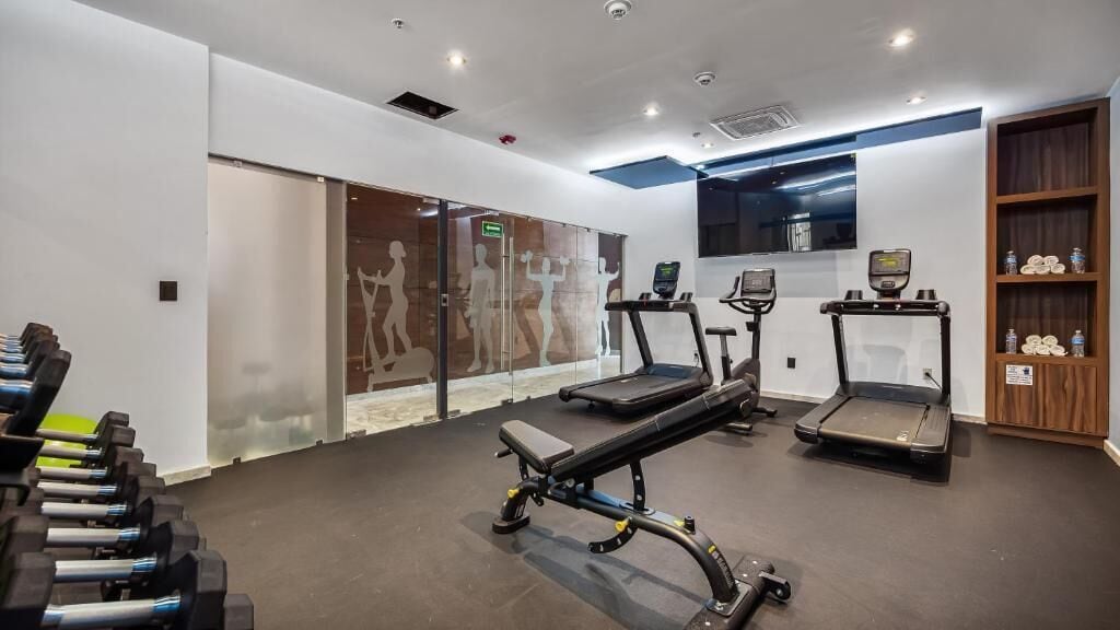 A gym with treadmills, a bench press, and dumbbells.