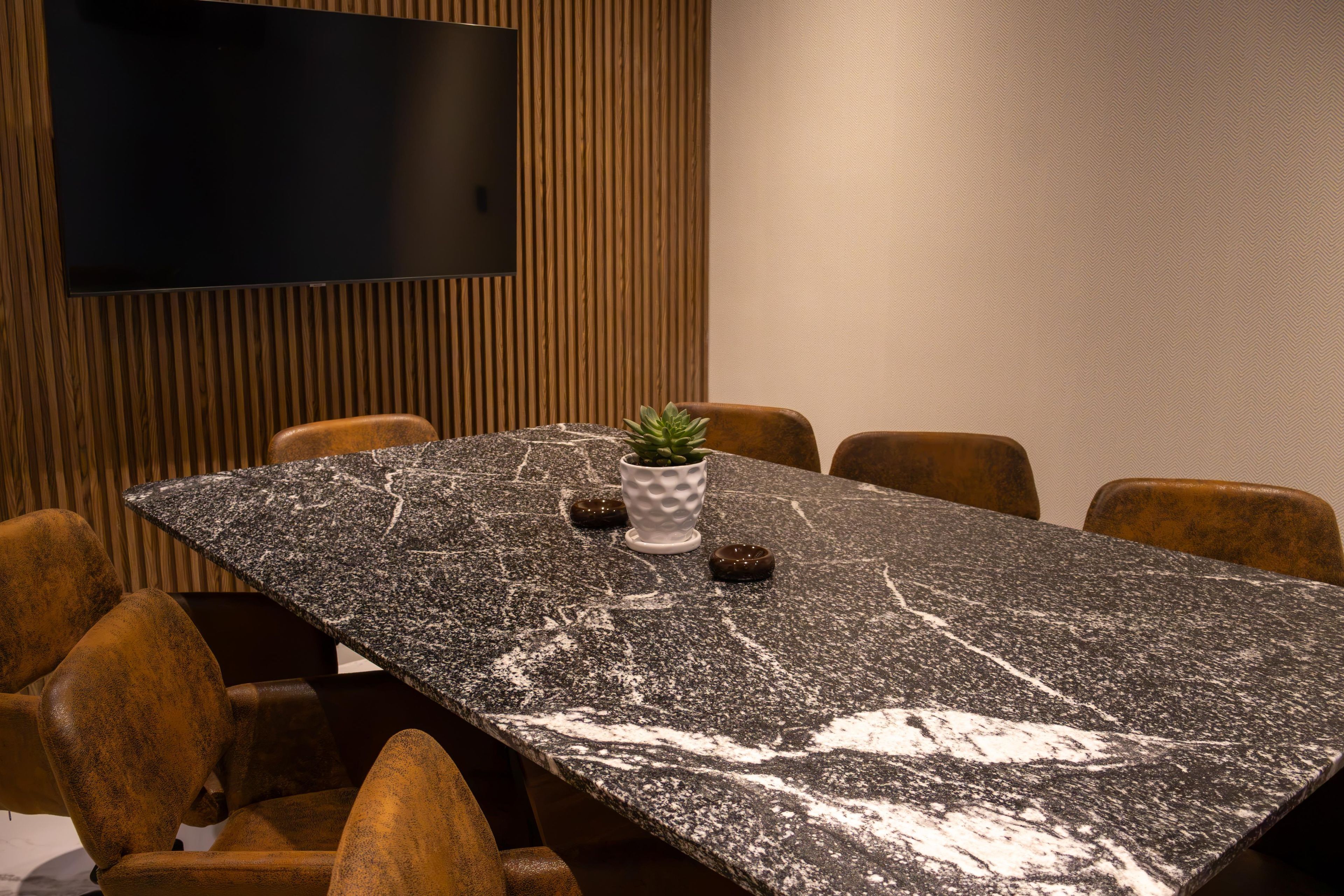 A conference room with a long table, chairs, a potted plant, and a flat-screen TV on the wall.