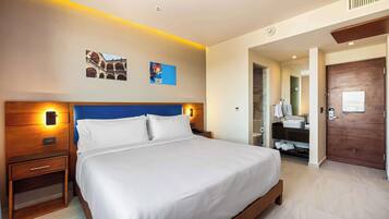 Habitación de hotel con una cama grande, cabecera de madera, mesitas de noche, baño con lavamanos y espejo, y dos obras de arte colgadas en la pared.