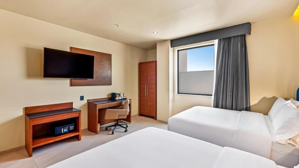 A hotel room with two beds, a desk with a chair, a TV mounted on the wall, and a wardrobe.