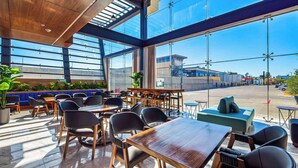A modern indoor dining area with large windows, wooden tables, and black chairs.