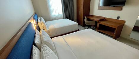 A hotel room with two beds, a desk, a chair, a TV, and a window with curtains.
