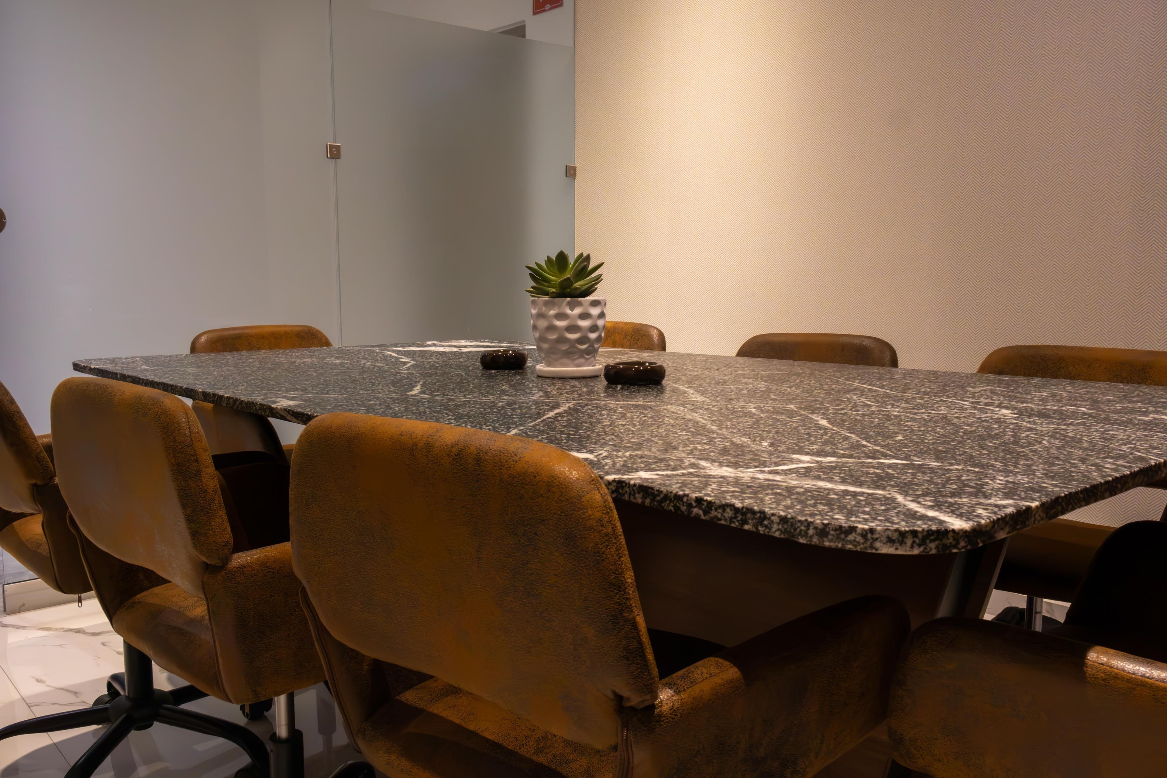 Een vergaderruimte met een marmeren tafel, bruine leren stoelen, een potplant en een gestructureerde wand.