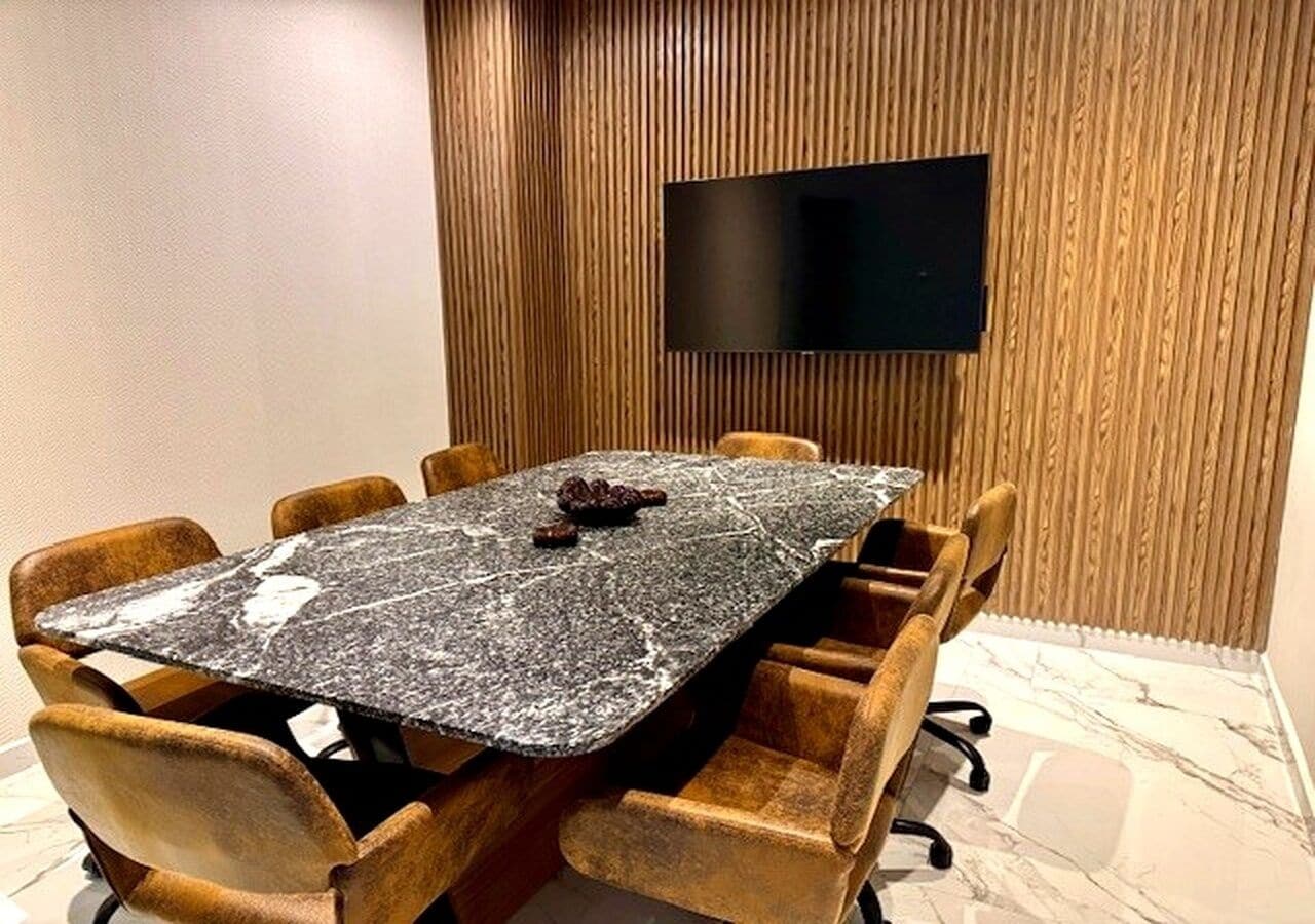A conference room with a marble table, wooden chairs, and a mounted TV on the wall.