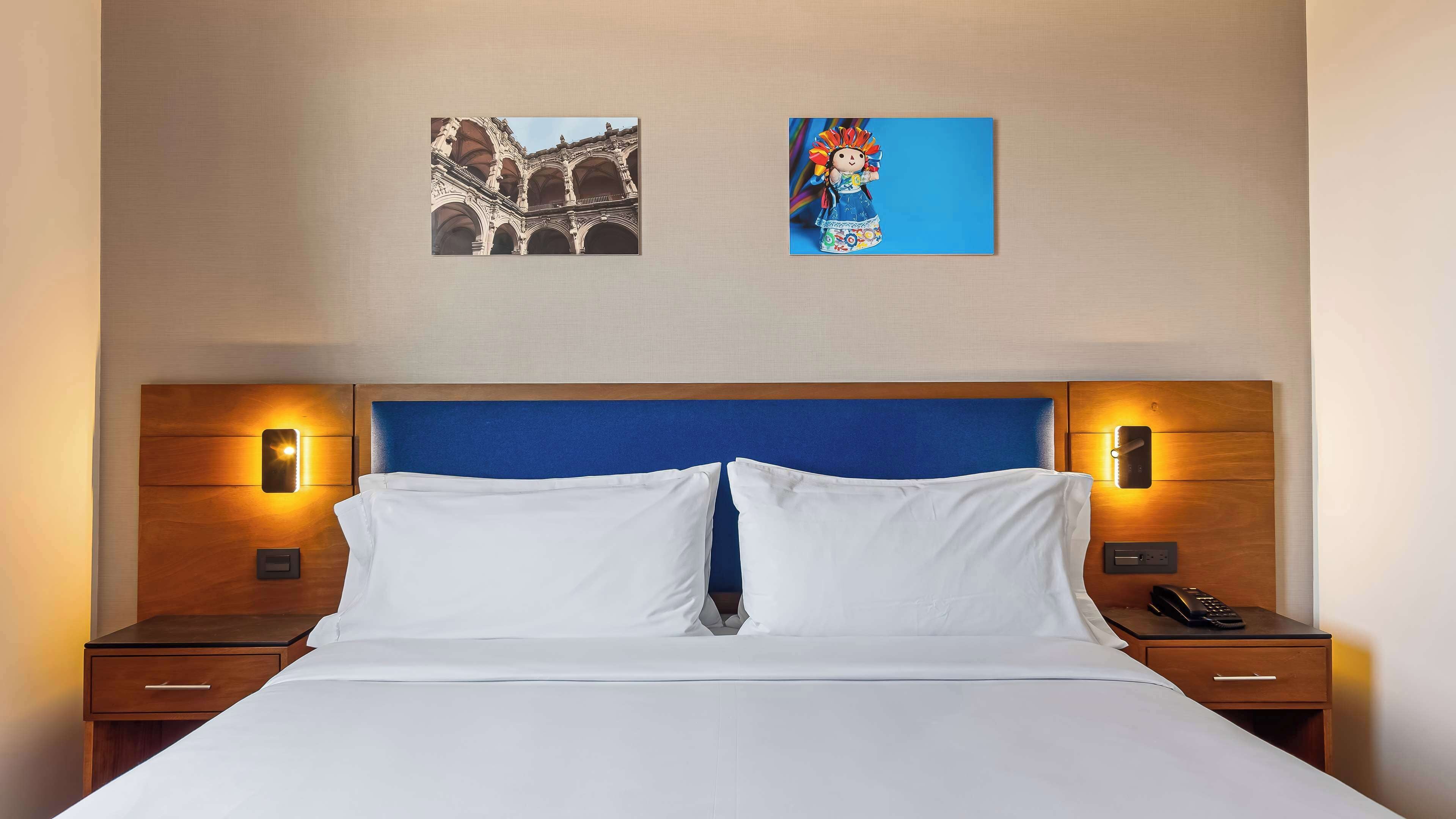 Ein Hotelzimmer mit einem großen Bett, zwei Nachttischen, einem Holz-Kopfteil und Wandleuchten.
