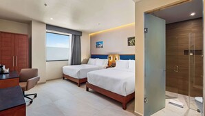 A hotel room with two beds, a desk, a chair, a wardrobe, and a bathroom.