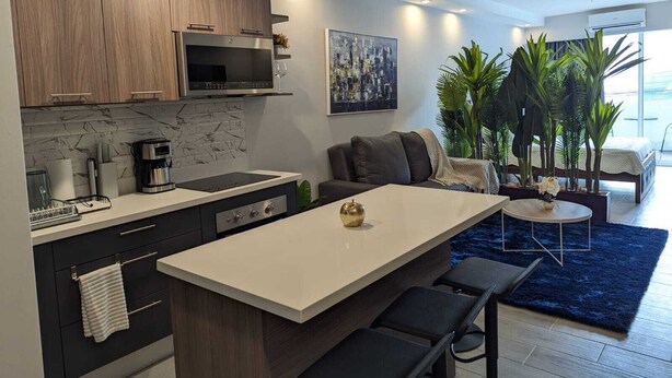 A modern kitchen with dark wood cabinets, a white countertop, and a central island with bar stools. - 113 Rocks, Perfect location for business and having everything within reach. (Heredia)