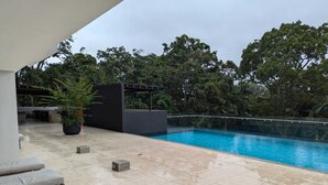 A modern outdoor pool area with a clear blue pool, tiled flooring, and a few lounge chairs. - 113 Rocks, Perfect location for business and having everything within reach. (Heredia)