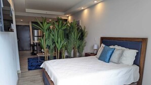 A bedroom with a large bed, a wooden headboard, a nightstand with a lamp, and a blue rug. - 113 Rocks, Perfect location for business and having everything within reach. (Heredia)