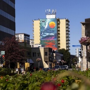 A building with a large mural of a landscape featuring a sun, moon, and waves. - Loft 302 | Rooftop | Downtown (Rimouski)