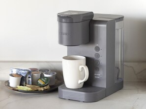 Una màquina de cafè Keurig amb una tassa blanca i càpsules de cafè damunt un taulell de cuina.