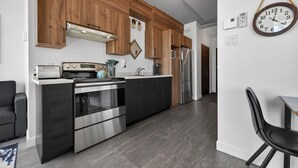 A modern kitchen with wooden cabinets, stainless steel appliances, and a dining area with a black chair.
