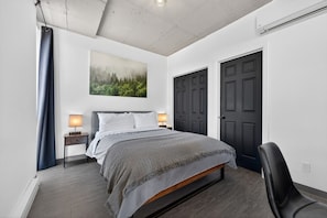 Un dormitorio con cama, lámparas de noche, una puerta oscura y un cuadro en la pared.