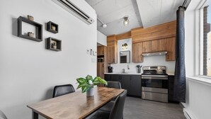 A modern kitchen with wooden cabinets, stainless steel appliances, and a dining area with a wooden table and chairs. - Loft 305 | Rooftop | Downtown (Rimouski)