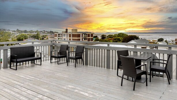 Eine Terrasse mit Sitzgelegenheiten und Blick auf den Sonnenuntergang über dem Wasser.