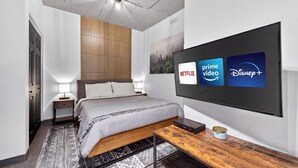 A modern hotel room with a bed, bedside tables, a TV displaying streaming services, and a wooden side table. - Loft 305 | Rooftop | Downtown (Rimouski)